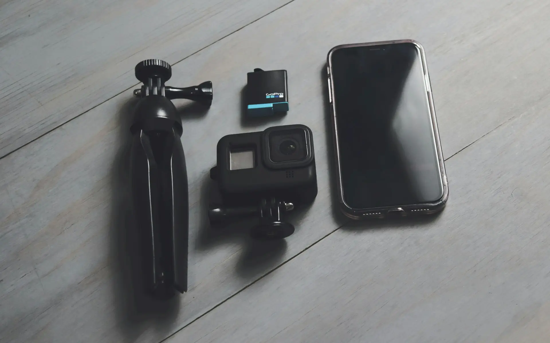 A cell phone, camera, and tripod sitting on a wooden floor